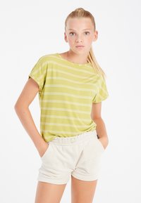 Maglietta a righe verde chiaro con maniche corte abbinata a pantaloni corti in crema con texture. La maglietta ha una vestibilità comoda e un collo rotondo.