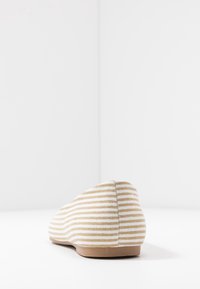 Randig platt sko i beige och vit tyg med rund tå, låg profil och en texturerad yta. Gummisula med minimal klack.