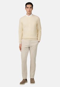 Jasnokremowy sweter, z okrągłym dekoltem, żebrowanymi mankietami, połączony z beżowymi spodniami i taupe wsuwanymi butami. Prosty, czysty design z neutralnymi kolorami.