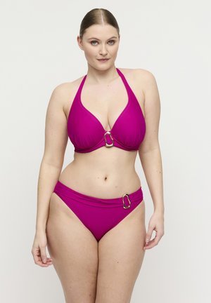 Vrouw draagt een magenta halter-bikini met gouden gespaccents op top en broekje, staand tegen een effen lichte achtergrond.