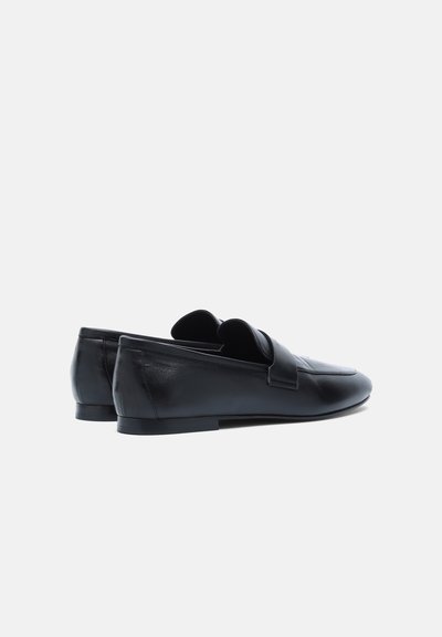 Paire de mocassins noirs en cuir sans lacets, talons bas, bouts arrondis et large sangle sur le dessus, vus de profil arrière.