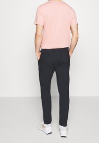 Lichtroze T-shirt met korte mouwen, donkere broek, witte sneakers met grijze accenten, nauwsluitend ontwerp, zichtbare achterzakken, gladde textuur.