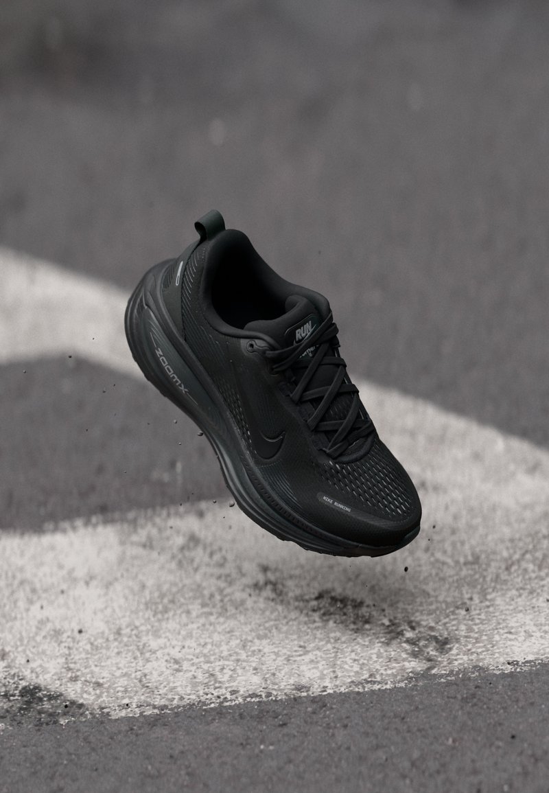 Chaussure de course noire Nike en suspension au-dessus de l'asphalte avec un marquage blanc au sol, mettant en avant un design léger et le mouvement.