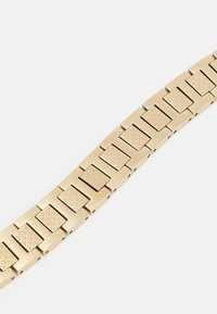 Bracelet en métal couleur or présentant des maillons rectangulaires avec des motifs géométriques en relief, une texture lisse et une finition brillante.