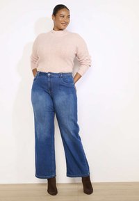 Roosa kudumissviiter, millel on ümar kaelus, koos kõrge talje ja laia säärega siniste teksadega. Pruunid pahkluuni saapad täiendavad lõdva riietuse.