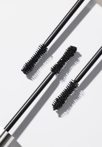 Trois goupillons de mascara noirs avec des poils texturés, chacun légèrement différent en longueur, positionnés sur un fond blanc.
