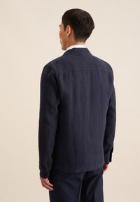 Camicia button-up in lino blu navy con colletto, maniche lunghe e polsini con bottone. Presenta una schiena a taglio dritto e dettagli di cucitura minimi.