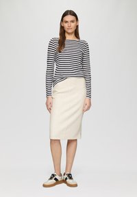Haut à manches longues rayé bleu marine et blanc associé à une jupe crayon beige clair et des baskets bicolores avec des accents noirs.