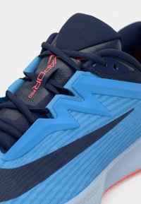 Sininen urheilukenkä, jossa on tekstuuripintainen verkkopinta, kontrastoivat tummansiniset yksityiskohdat, sahalaitakuviot ja joustava kumipohja.