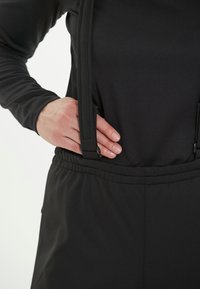 Musta vaate, jossa on säädettävät olkaimet ja elastinen vyötärö. Suora pinta, puhtaat linjat ja istuva muotoilu.