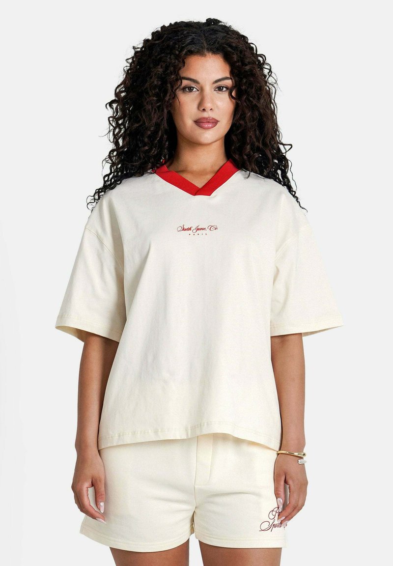 Camiseta de algodón blanca con escote en V rojo y logotipo bordado, combinada con pantalones cortos de algodón blancos que cuentan con un pequeño detalle bordado.