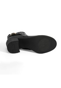 Schwarze Lederankelstiefel mit einem strukturierten Seitenpaneel und goldenen Hardware-Details. Dicke Gummisohle mit einer flachen, glatten Oberfläche für guten Halt.