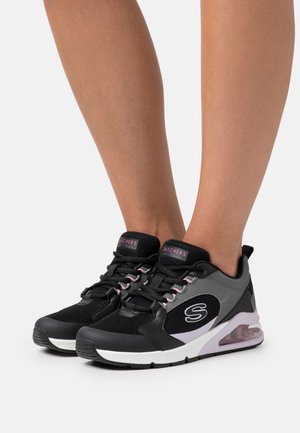 Black and gray athletic shoes with mesh and synthetic fabric, featuring a padded collar, laces, and a visible air cushioning unit.