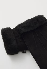 Svarta handskar i mocka, med en fluffig pälsmanchet och vertikala sömdetaljer, samt en liten tag fäst.