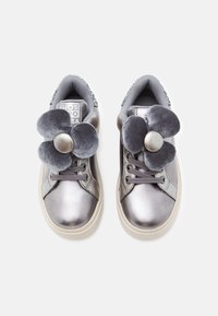 Zapatillas metálicas plateadas de tamaño infantil con cordones grises y grandes decoraciones de flores de terciopelo gris en la parte superior, sobre un fondo blanco.