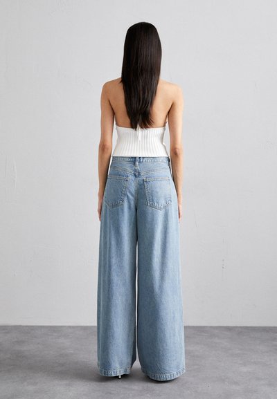 White ribbed crop top and wide-leg light blue denim trousers. The trousers feature a high waist, two back pockets, and a relaxed fit.