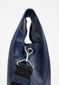 Námornícky modrá kožená taška s jemnou textúrou, zaobleným vrchom a striebornými doplnkami. Má klips a čierny nastaviteľný popruh.