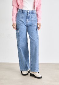 Lyseblå høytlivede denim cargo bukser med sidelommer, vide ben og en falmet finish, sammen med kremfargede loafers.