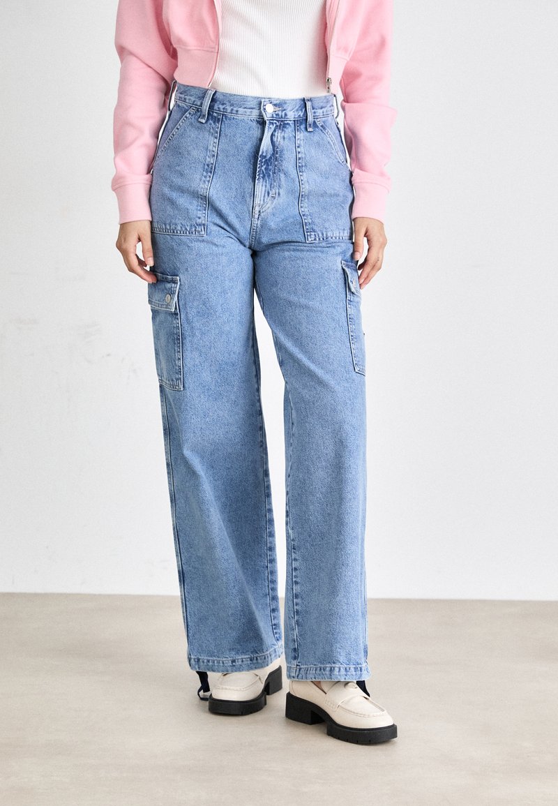 Lyseblå høytlivede denim cargo bukser med sidelommer, vide ben og en falmet finish, sammen med kremfargede loafers.