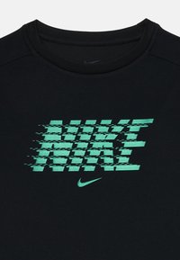Must värv ja lühikesed varrukad T-särk, millel on tekstureeritud, moonutatud roheline "NIKE" logo ja väike Nike swoosh, ümar kaelus.