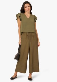 Haut vert olive avec des manches à volants et un décolleté en V, associé à un pantalon large vert olive avec une taille élastique et un cordon de serrage. Sac à main noir.
