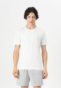 T-shirt en coton blanc avec un col rond et des manches courtes, associé à un short rayé gris et blanc. Les détails incluent un petit logo sur la poitrine.