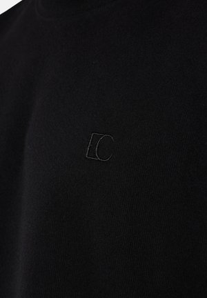 Schwarzer Stoff mit dezent eingesticktem Logo, das ineinander übergehende Buchstaben "E" und "C" in passendem schwarzem Garn auf der Brust zeigt.