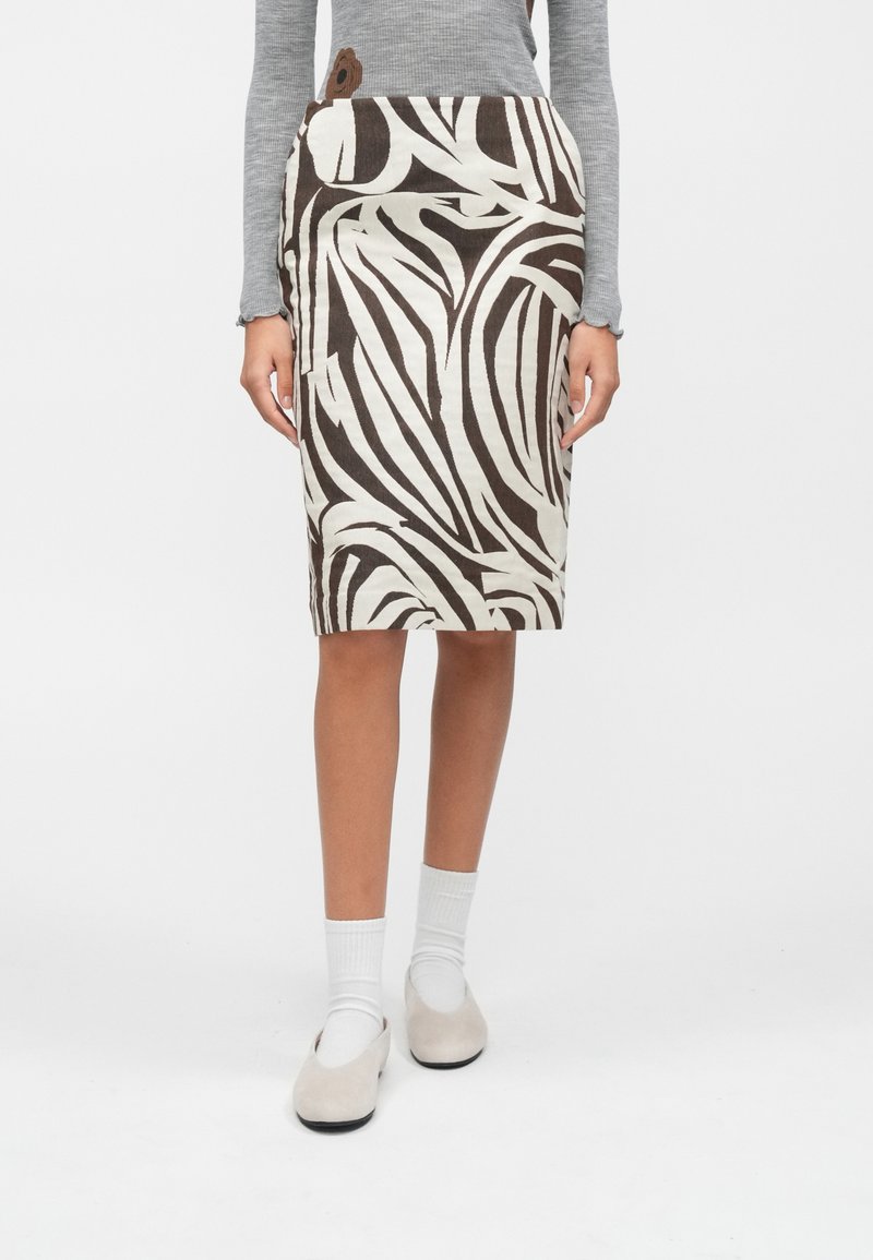 Persoană purtând o fustă până la genunchi cu dungi abstracte de zebre în maro și alb, bluză cu mâneci lungi gri, șosete albe și pantofi bej fără toc.