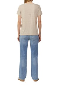 Beige en crèmekleurig gestreept T-shirt met korte mouwen, gecombineerd met lichtblauwe uitlopende jeans. De outfit heeft een ontspannen pasvorm en een zachte textuur.