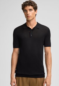 Polo shirt nera a maniche corte in un tessuto leggero. Caratterizzato da un colletto classico, tre bottoni e orlo e polsini a coste.