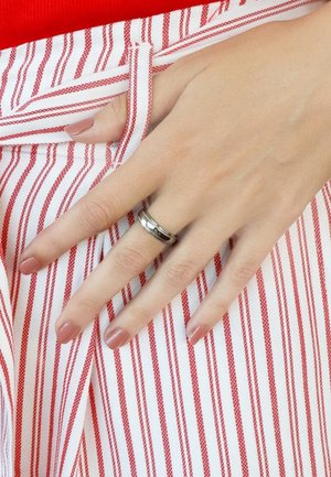Zilveren ringen met een gedraaide ontwerp en lineaire accenten, gedragen aan een hand die rust op een rood-wit gestreepte stof. De nagels zijn neutraal van kleur.