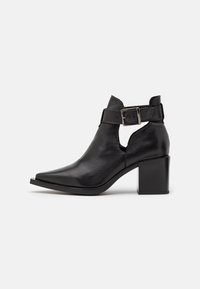 Schwarze Leder-Ankle-Boots mit spitzer Zehenform, ausgeschnittenen Seiten und einer Schnallenriemen. Mit einem klobigen Blockabsatz und glatter Textur.