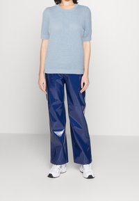 Suéter de punto texturizado de manga corta en azul claro combinado con pantalones de pierna ancha en azul marino brillantes. La modelo lleva deportivas blancas.