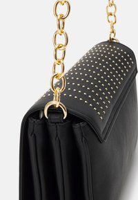 Borsa in pelle nera con design a borchie dorate e tracolla a catena dorata. La borsa presenta una chiusura a patta e una forma strutturata.