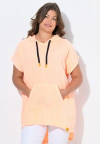 Tunic con cappuccio arancione chiaro realizzata in tessuto testurizzato, dotata di tasca frontale, maniche corte e lacci neri con accenti arancioni.