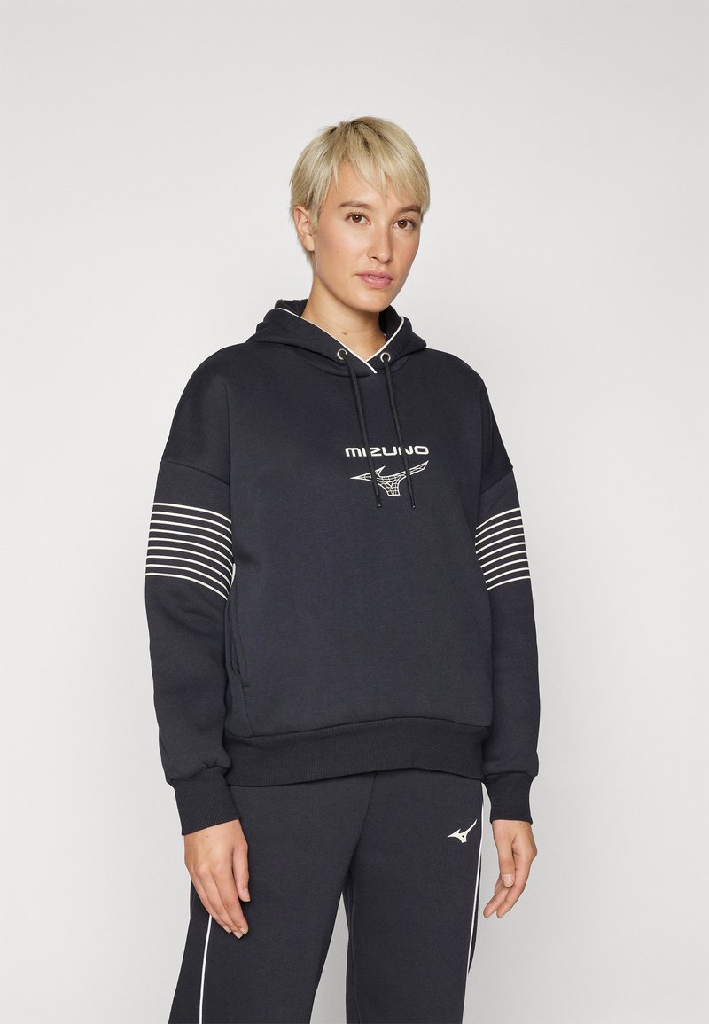 Svart hettegenser med logo, med hvite striper på ermene. Stoffet ser mykt og koselig ut. Kombinert med matchende svarte bukser.