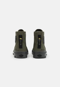 Bottines vertes avec une tige en tissu, semelle en caoutchouc noir et accents de logo proéminents. Comprend des languettes pour un enfilage facile.
