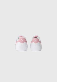 Une paire de baskets Puma blanches et roses vues de derrière sur un fond clair.