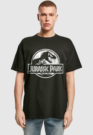 Black cotton t-shirt featuring a vintage Jurassic Park logo graphic in white, with a round shape and short sleeves. Textured print detail.
