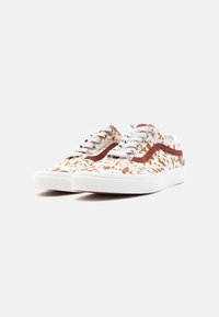 Paire de baskets basses blanches avec motif en cuir de vache marron et bande latérale marron, lacets blancs et semelles en caoutchouc blanches sur fond uni.