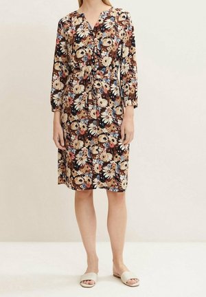 Knielange bloemenjurk met driekwartmouwen, knoopsluiting aan de voorkant en tailleband, gedragen met beige open-toe slippers.