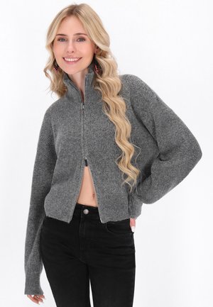 Grijze cropped sweater met rits en lange mouwen, gemaakt van textielstof. Gecombineerd met zwarte hoge taille jeans.