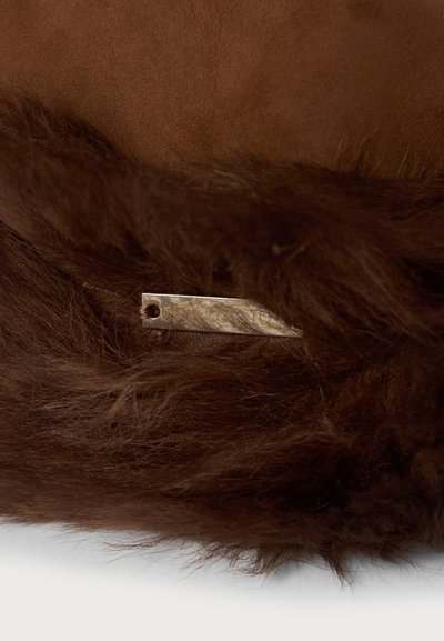 Nahaufnahme von braunem Fellstoff mit einem kleinen, metallischen Dior-Tag, der teilweise zwischen den Fasern verborgen ist.