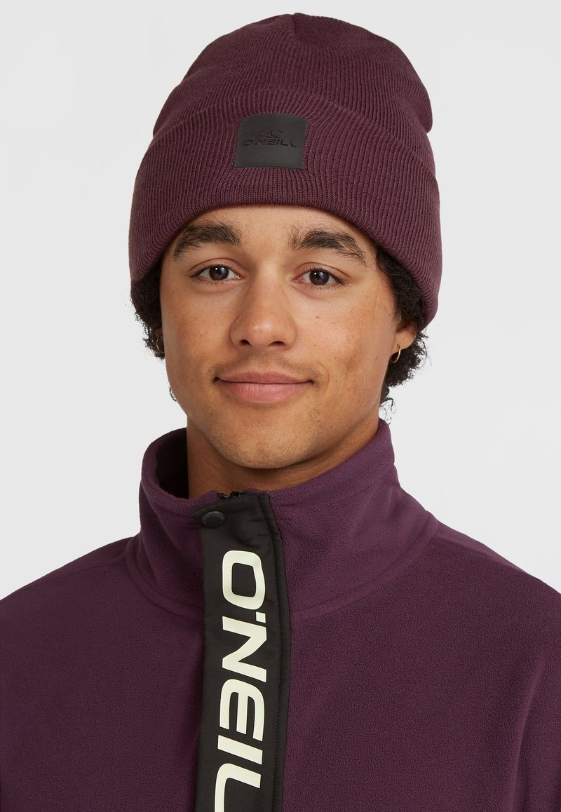 Maroon beanie with ribbed texture and black logo patch; purple fleece jacket with a zip and contrasting black zipper detailing.