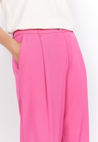 Pantalons plissés roses avec poches latérales ; fabriqués dans un tissu lisse et léger ; dotés d'une taille avec fermeture à bouton.