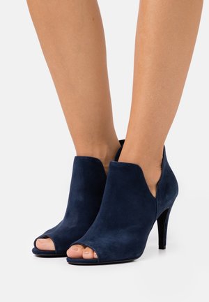 Tmavě modré semišové kotníkové boty s otevřenou špičkou a elegantním designem, které mají vysoký podpatek a výřez po stranách.
