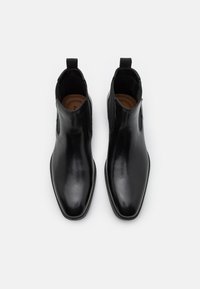 Černé kožené chelsea boty s hladkým povrchem, elastickými bočními panely a poutky pro snadné obutí. Špičatá špička a ploché podrážky.
