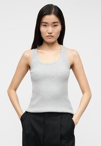 Grå ribstrikket tanktop med rund halsudskæring og brede skulderstropper, kombineret med sorte bukser, der har en tætsiddende silhuet og minimal tekstur.