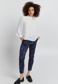 Hvid langærmet bluse med samlingdetaljer, parret med mønstrede navy og lilla leopardmønstrede bukser og sorte loafers.