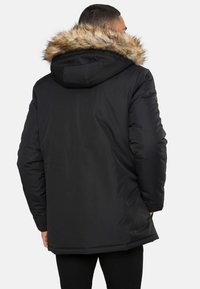 Černá prošívaná bunda s kapucí lemovanou kožešinou. Má elegantní design, matný povrch a dlouhý střih, vhodná pro chladné počasí.